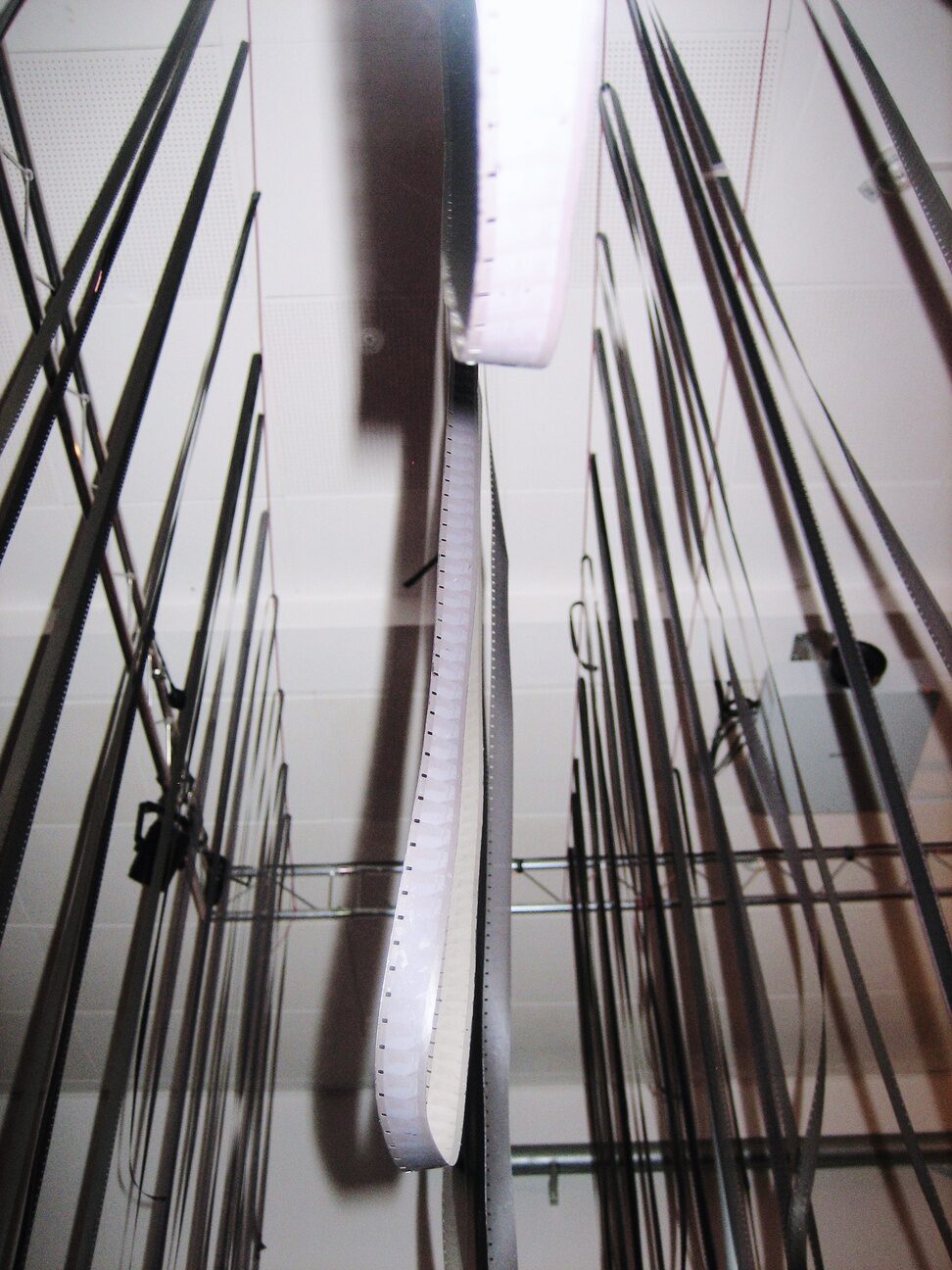 Long strips of freshly hand-developed 16mm film hanging from a rack to dry
