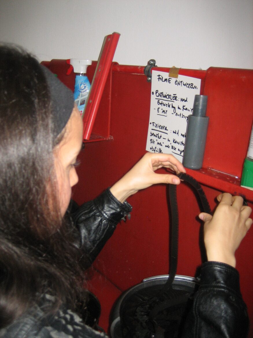 Processing 16mm film by hand at a red darkroom station, next to handwritten developing instructions