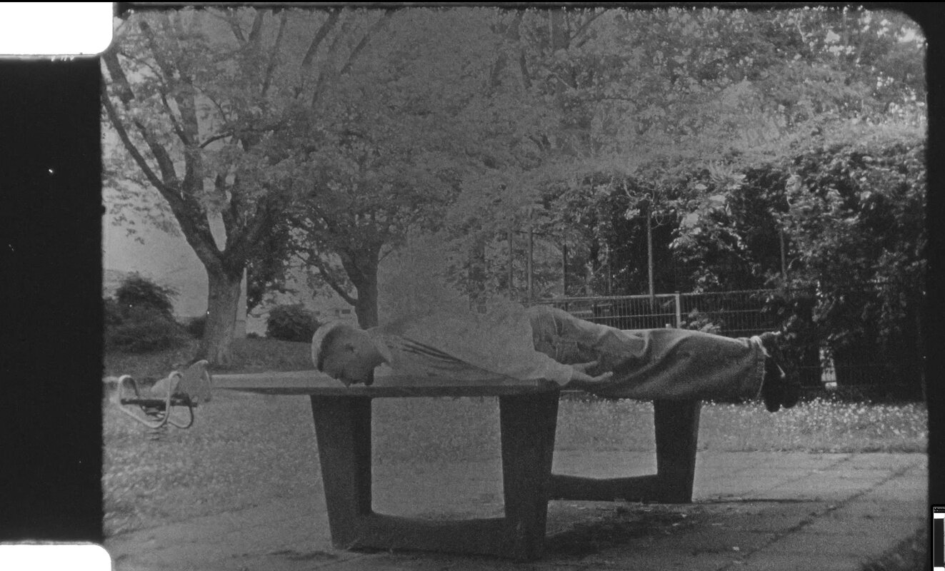 Figure lying across a concrete bench in a park