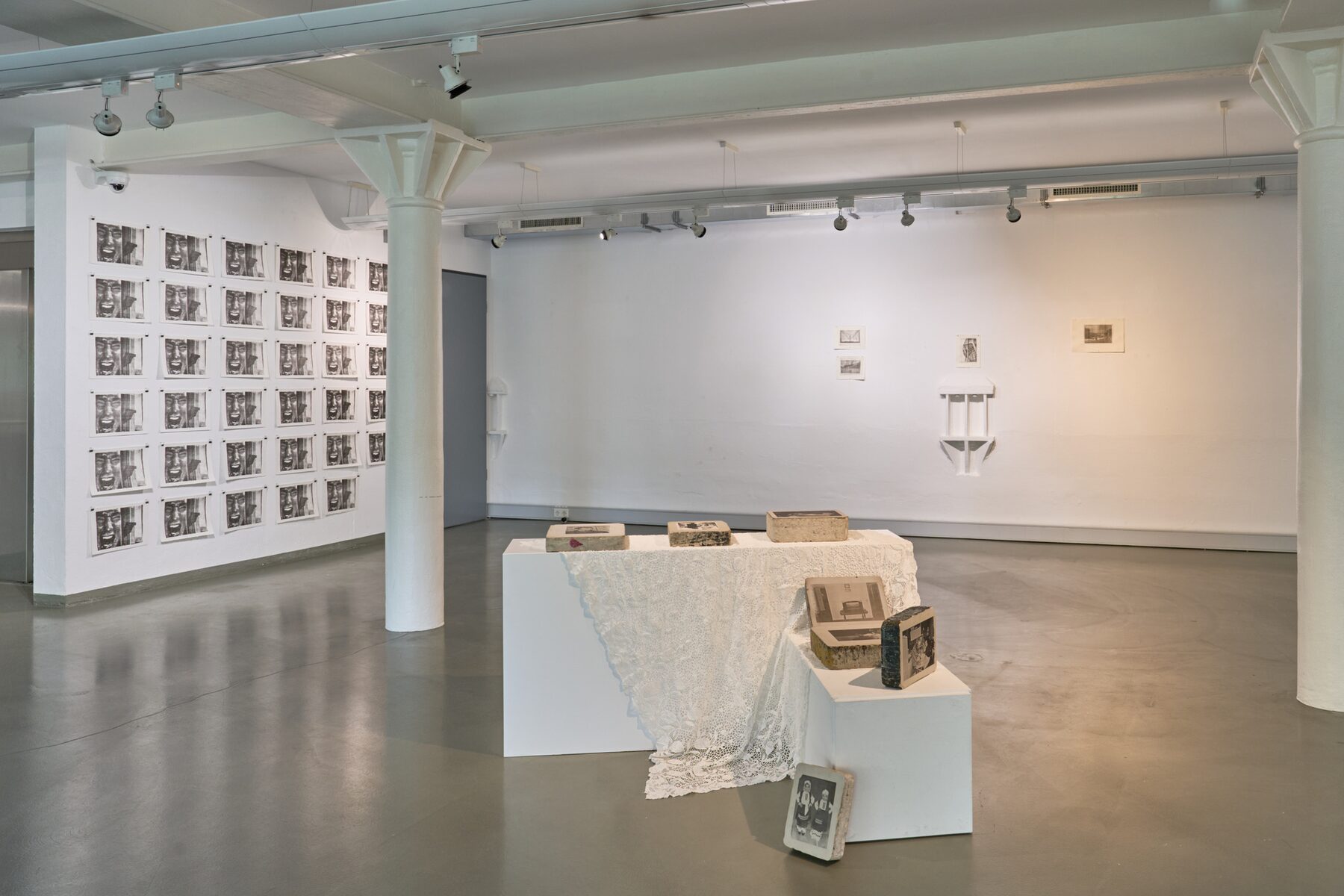 Gallery installation with lithographic stones arranged on lace-covered plinths